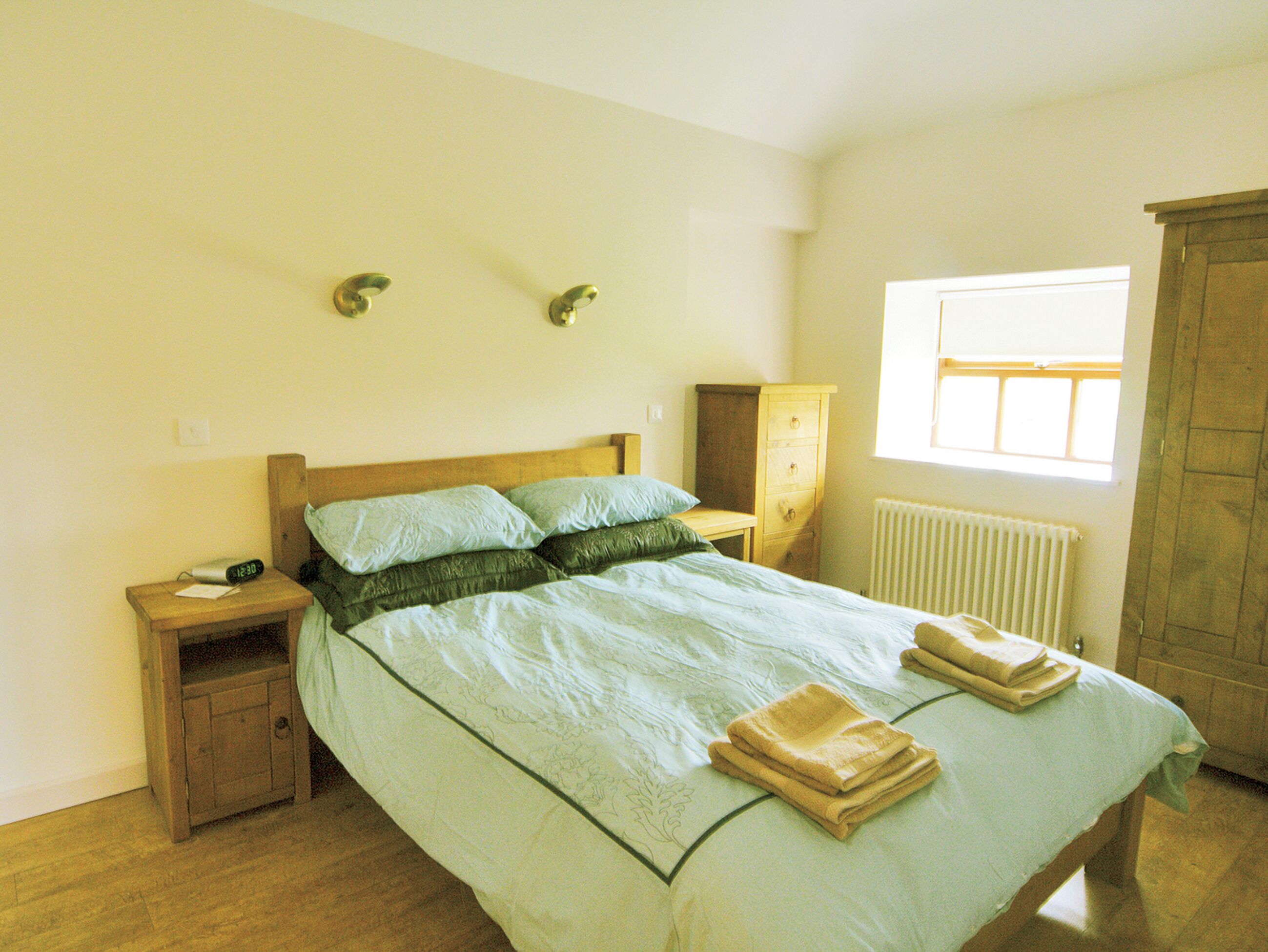 Quarto com cama, mesa de cabeceira, cômoda e janela.