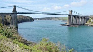 Un puente colgante sobre un río, con pilares de piedra y cielo despejado.