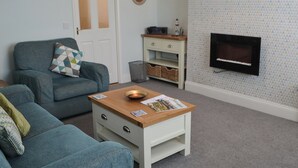 A living room with a blue sofa, a wooden coffee table, a television on the wall, and a patterned wallpaper.