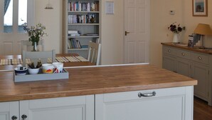 A kitchen with a wooden countertop, white cabinets, a bookshelf, and a dining area with a table and chairs.