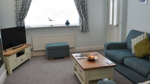A living room with a television, a sofa, a coffee table, and a window with curtains.