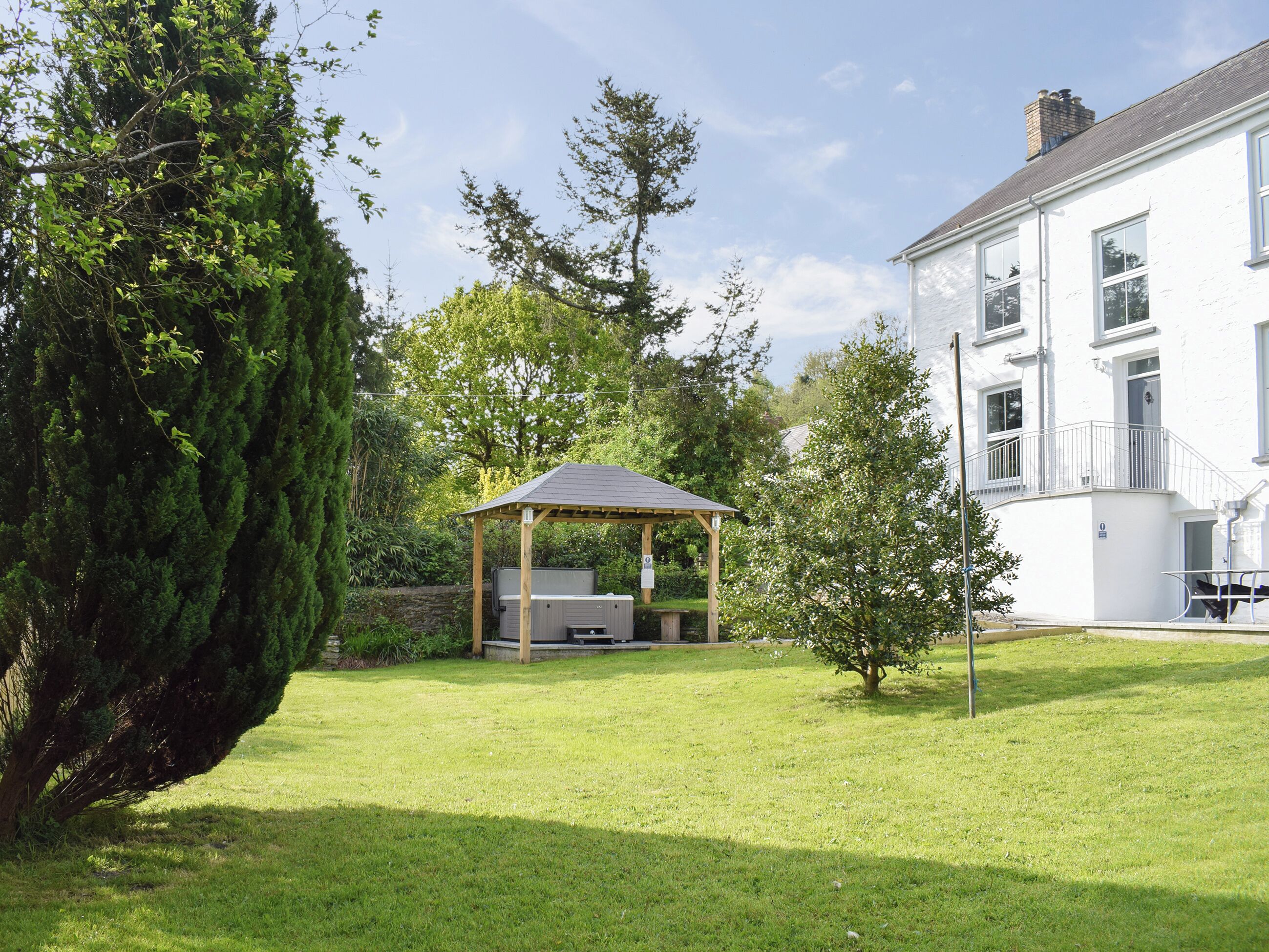 A well-maintained garden with a wooden gazebo, a large tree, and a white building with multiple windows and a balcony.