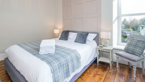 A neatly made bed with a grey and white checkered blanket, a grey upholstered bench, and a white nightstand with a lamp. - 4 bedroom accommodation in Abercych, near Cardigan (Abercych, near Cardigan)
