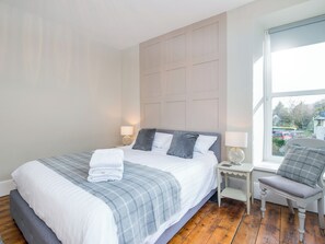 A neatly made bed with a grey and white checkered blanket, a grey upholstered bench, and a white nightstand with a lamp. - 4 bedroom accommodation in Abercych, near Cardigan (Abercych, near Cardigan)
