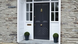 A black door with a brass knocker, flanked by two potted plants and two wall-mounted lanterns. - 4 bedroom accommodation in Abercych, near Cardigan (Abercych, near Cardigan)