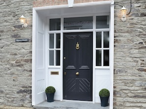 A black door with a brass knocker, flanked by two potted plants and two wall-mounted lanterns. - 4 bedroom accommodation in Abercych, near Cardigan (Abercych, near Cardigan)