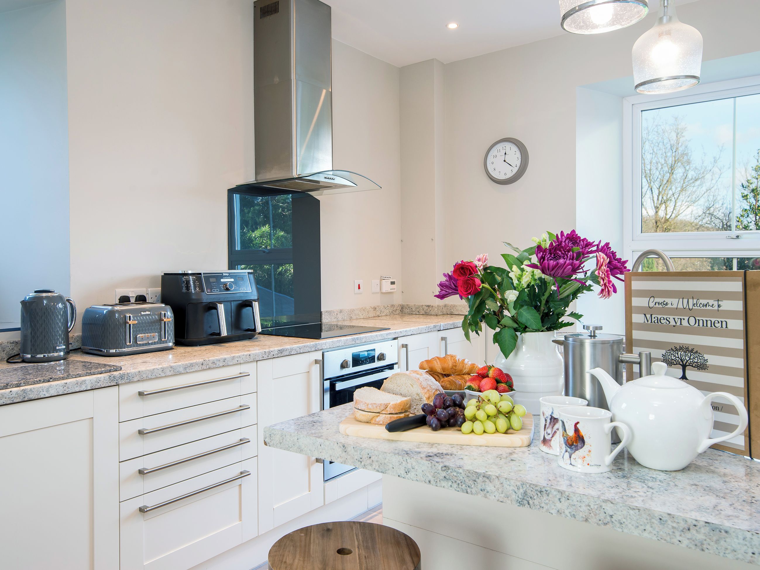 A modern kitchen with a built-in oven, a coffee maker, a toaster, and a clock on the wall.