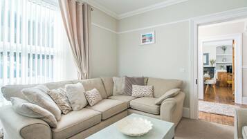 A living room with a beige sectional sofa, a light-colored coffee table, and a door leading to a dining area.