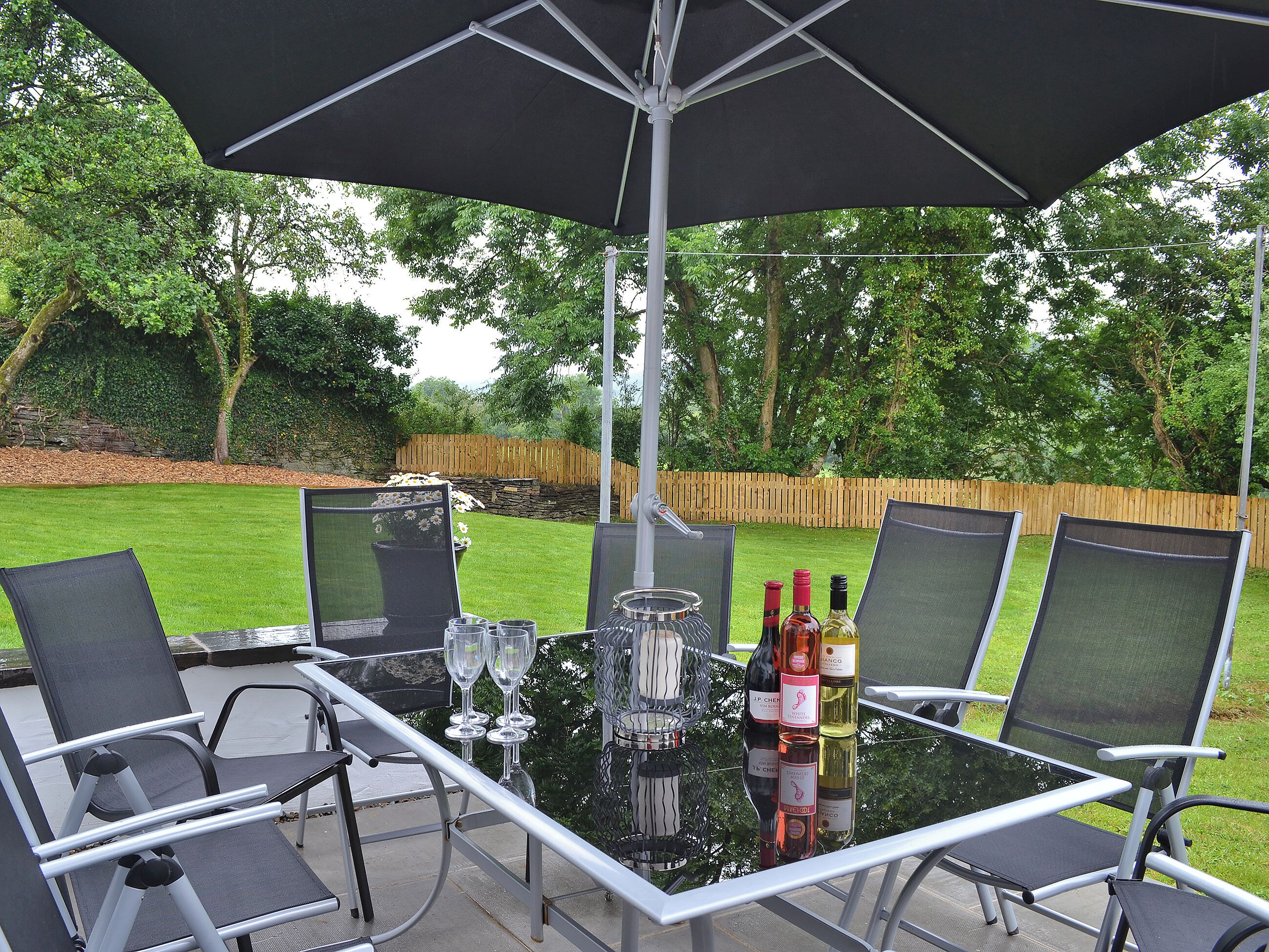 An outdoor patio with a glass table, four chairs, and a large umbrella.