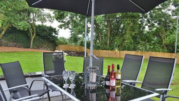 An outdoor patio with a glass table, four chairs, and a large umbrella.
