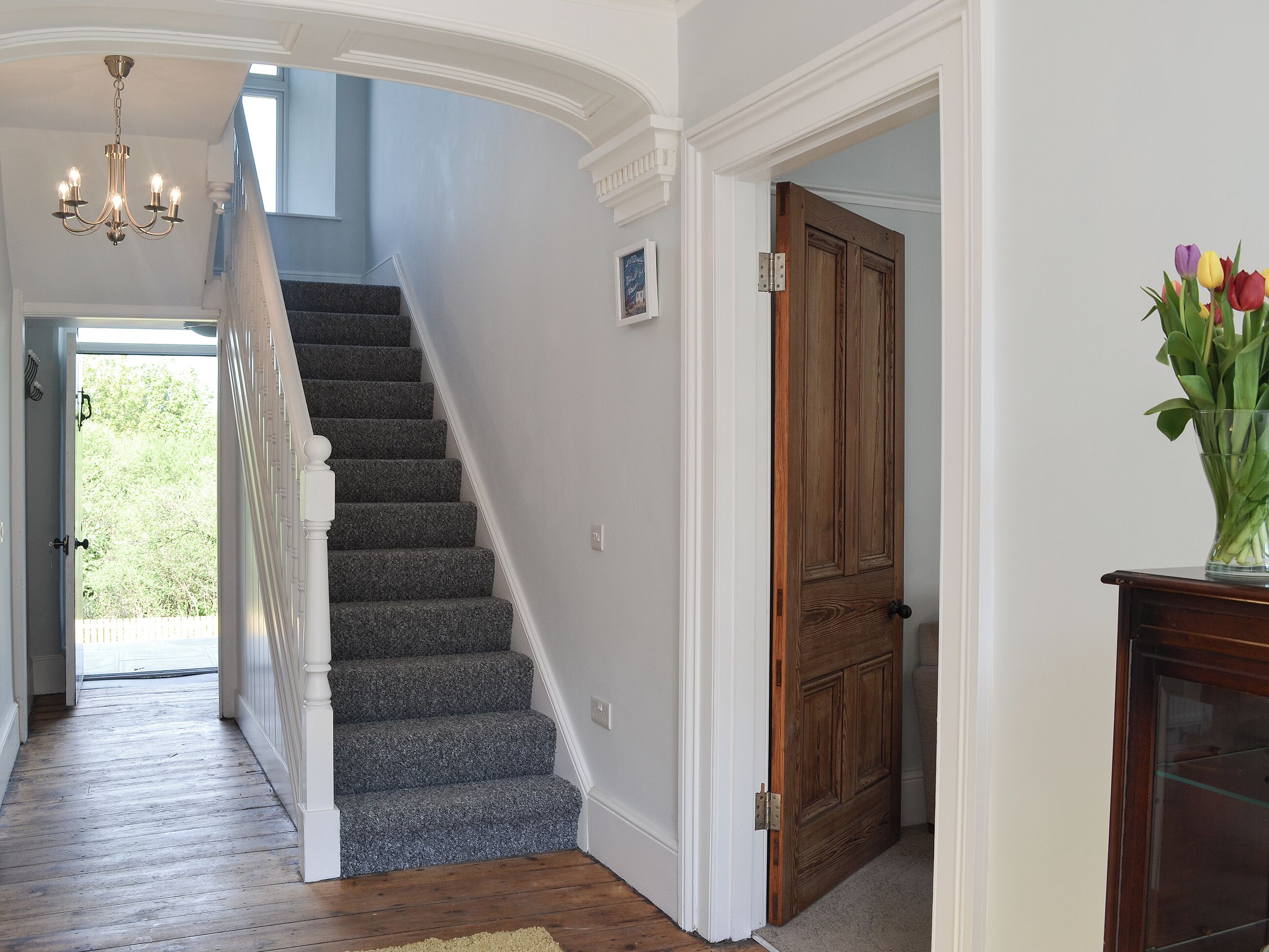A staircase with carpeted steps leading to a door, a chandelier, and a vase with flowers.