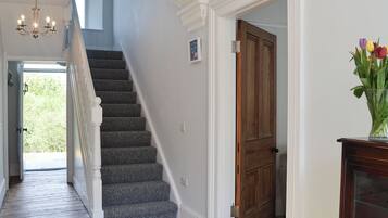 A staircase with carpeted steps leading to a door, a chandelier, and a vase with flowers.