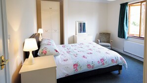 Een slaapkamer met een bed, nachtkastjes, een kaptafel, een stoel, een raam met gordijnen en een plafondlamp.