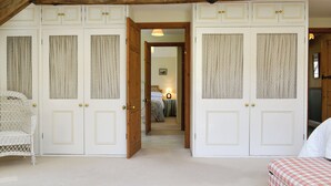 Une chambre avec un grand lit, un fauteuil en osier et une armoire agrémentée de rideaux à motifs.