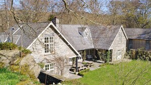 Un bâtiment en pierre comprenant plusieurs pièces, une cheminée en pierre et une cour verdoyante agrémentée de fleurs.