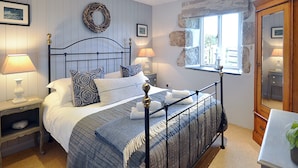 Une chambre à coucher comprenant un lit, deux tables de chevet, une commode, une fenêtre avec un cadre en pierre et un miroir.