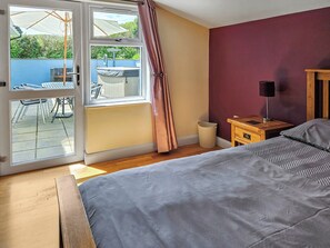 Une chambre à coucher comprenant un lit, une table de chevet, une lampe, une fenêtre avec des rideaux et donnant sur une terrasse extérieure.
