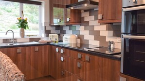 A modern kitchen with wooden cabinets, a built-in oven, a toaster, and a window with a view of greenery. - 3 bedroom accommodation in Dihewyd, near Aberaeron (Dihewyd, near Aberaeron)