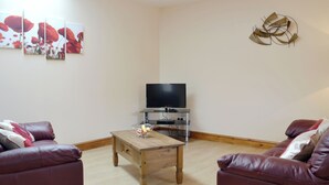 Un saló amb una taula de centre de fusta, dos sofàs de cuir, un televisor de pantalla plana sobre un suport i tres quadres emmarcats a la paret.