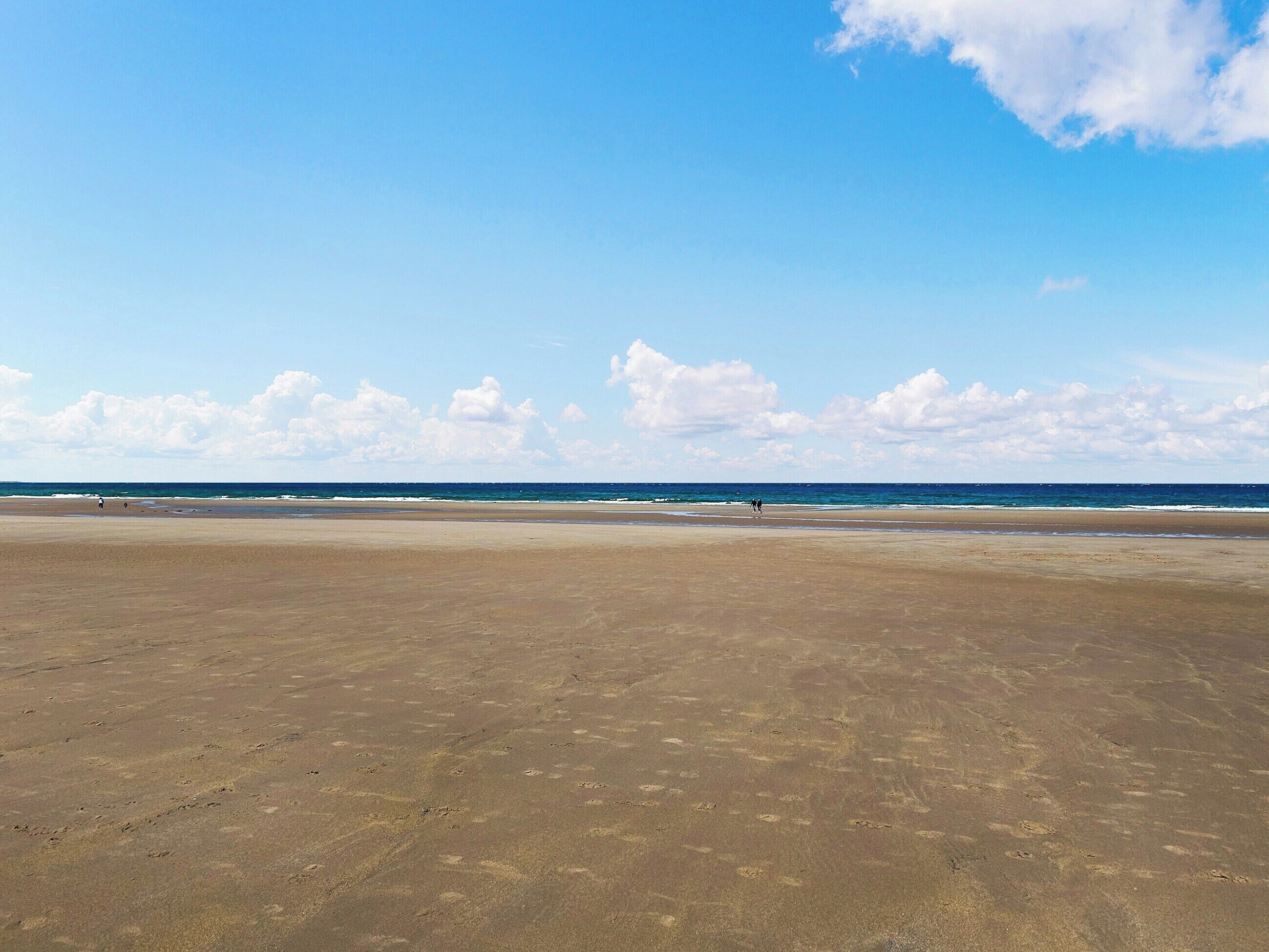 Ein weiter, offener Strand mit blauem Himmel und weiter Sicht auf den Ozean.
