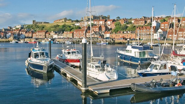 A marina with boats docked, a wooden pier, and a town with red-roofed buildings in the background. - 1 bedroom accommodation in Whitby (Whitby)