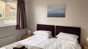 Une chambre avec un grand lit, une fenêtre avec des rideaux, une table de chevet avec une lampe et un tableau au mur.