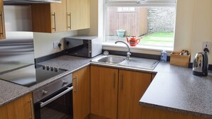 Une cuisine moderne avec des meubles en bois, une hotte de cuisine en acier inoxydable, un four à micro-ondes encastré et une fenêtre donnant sur le jardin.