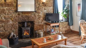 Ein gemütliches Wohnzimmer mit Kamin aus Stein, einem Flachbildfernseher auf einem Holzboden, einer bequemen Couch und einem Couchtisch mit Snacks.
