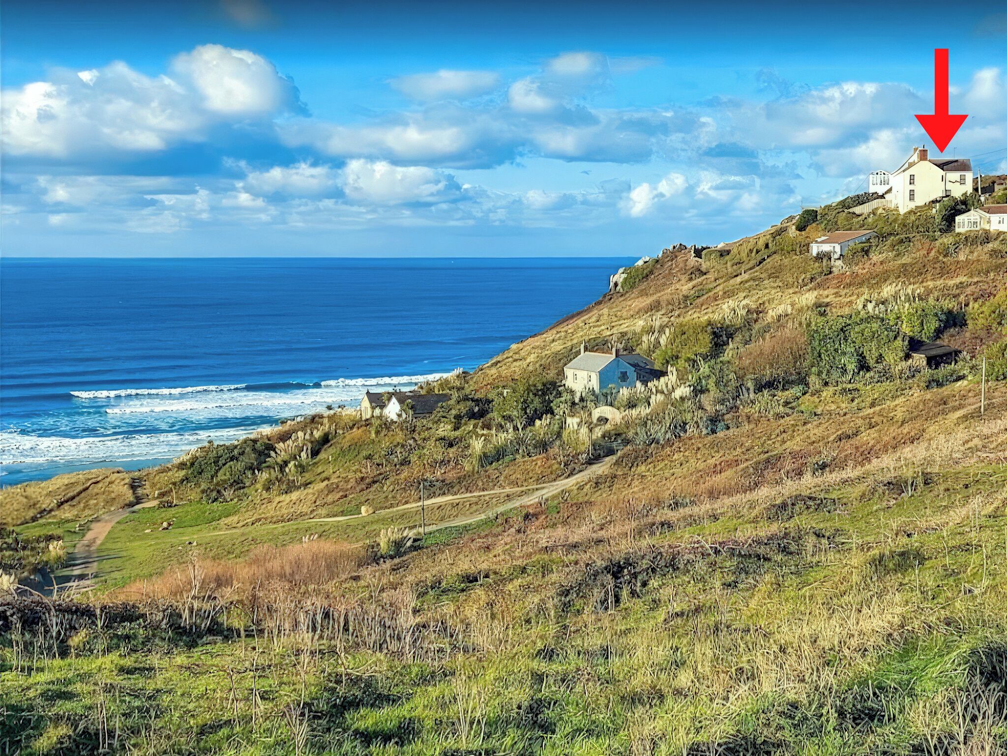 A coastal landscape with a house on a hillside overlooking the ocean.