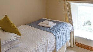 A neatly made bed with a blue and white duvet, a yellow pillow, and a folded white towel on the bed. - 3 bedroom accommodation in Bamburgh (Bamburgh)