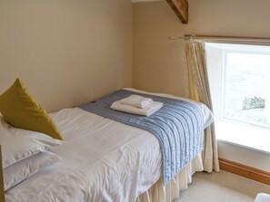 A neatly made bed with a blue and white duvet, a yellow pillow, and a folded white towel on the bed.