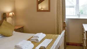 Et hotelværelse med seng, et natbord med lampe, et spejl og et vindue med gardiner.