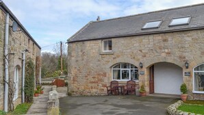 A stone building with a garage, a patio with chairs, and a small garden area. - 3 bedroom accommodation in Bamburgh (Bamburgh)