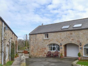 Une construction en pierre avec un garage, une terrasse avec des chaises et un petit jardin.