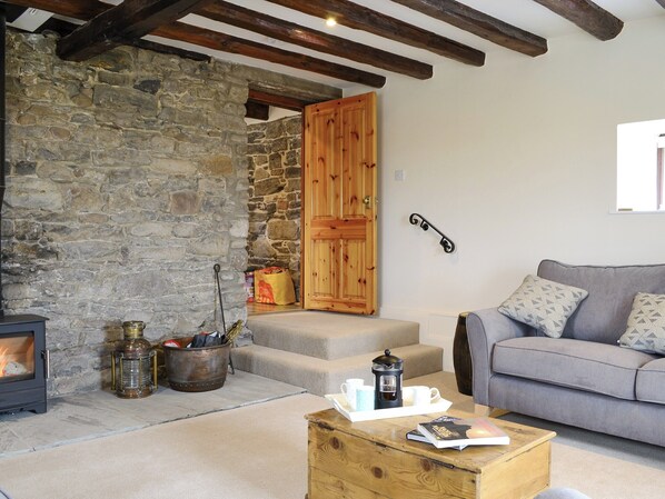 A cozy living room with a stone wall, a fireplace, a wooden door, a gray sofa, and a coffee table with books and a coffee pot.