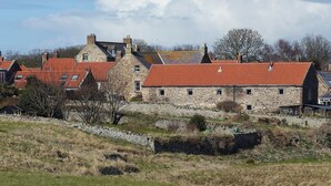 A stone building with red-tiled roofs, surrounded by a stone wall and grassy area. - 4 bedroom accommodation in Holy Island, near Berwick-upon-Tweed (Holy Island, near Berwick-upon-Tweed)