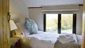 Un dormitorio con una cama, una mesita de noche, una lámpara, una ventana con vistas a árboles y una puerta.