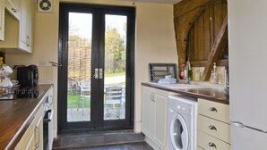Una cocina con lavadora, cafetera y un área de comedor visible a través de una puerta de cristal.