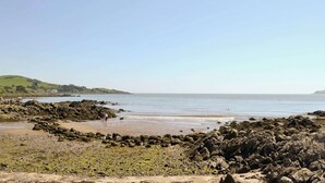 Een rotsachtig strand met een helder uitzicht op de zee en heuvels in de verte.