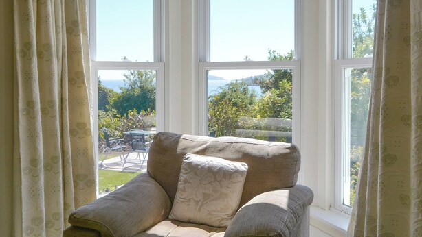 Een kamer met een beige fauteuil bij een groot raam met uitzicht op een tuin en bergen.