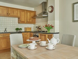 A kitchen with wooden cabinets, a tiled backsplash, a clock, a vase with flowers, and a dining table set with white cups and plates. - 3 bedroom accommodation in Pickering (Pickering)