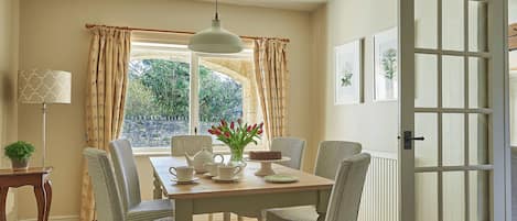A dining area with a table, chairs, a lamp, and a view through the window.