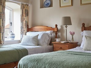 A bedroom with two beds, a bedside table with a lamp, a vase with flowers, and a window with curtains. - 3 bedroom accommodation in Pickering (Pickering)