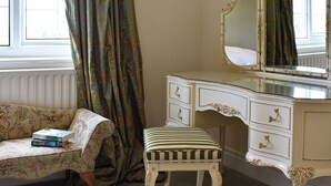 Une pièce avec une coiffeuse blanche, un miroir, un banc à rayures et une fenêtre avec des rideaux.