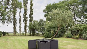 Un espace extérieur verdoyant avec une table carrée et quatre chaises, entouré d’arbres et d’un banc en bois.