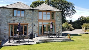 A stone building with a patio, outdoor seating, and a view of the surrounding landscape. - 6 bedroom accommodation in Tregoodwell, Camelford (Tregoodwell, Camelford)