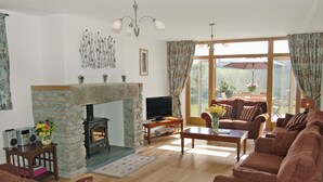 A living room with a stone fireplace, a television, and a sofa set. - 6 bedroom accommodation in Tregoodwell, Camelford (Tregoodwell, Camelford)