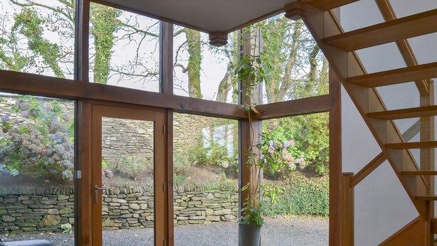 A room with large glass doors, a stone wall, a wooden ceiling, and a potted plant. - 6 bedroom accommodation in Tregoodwell, Camelford (Tregoodwell, Camelford)
