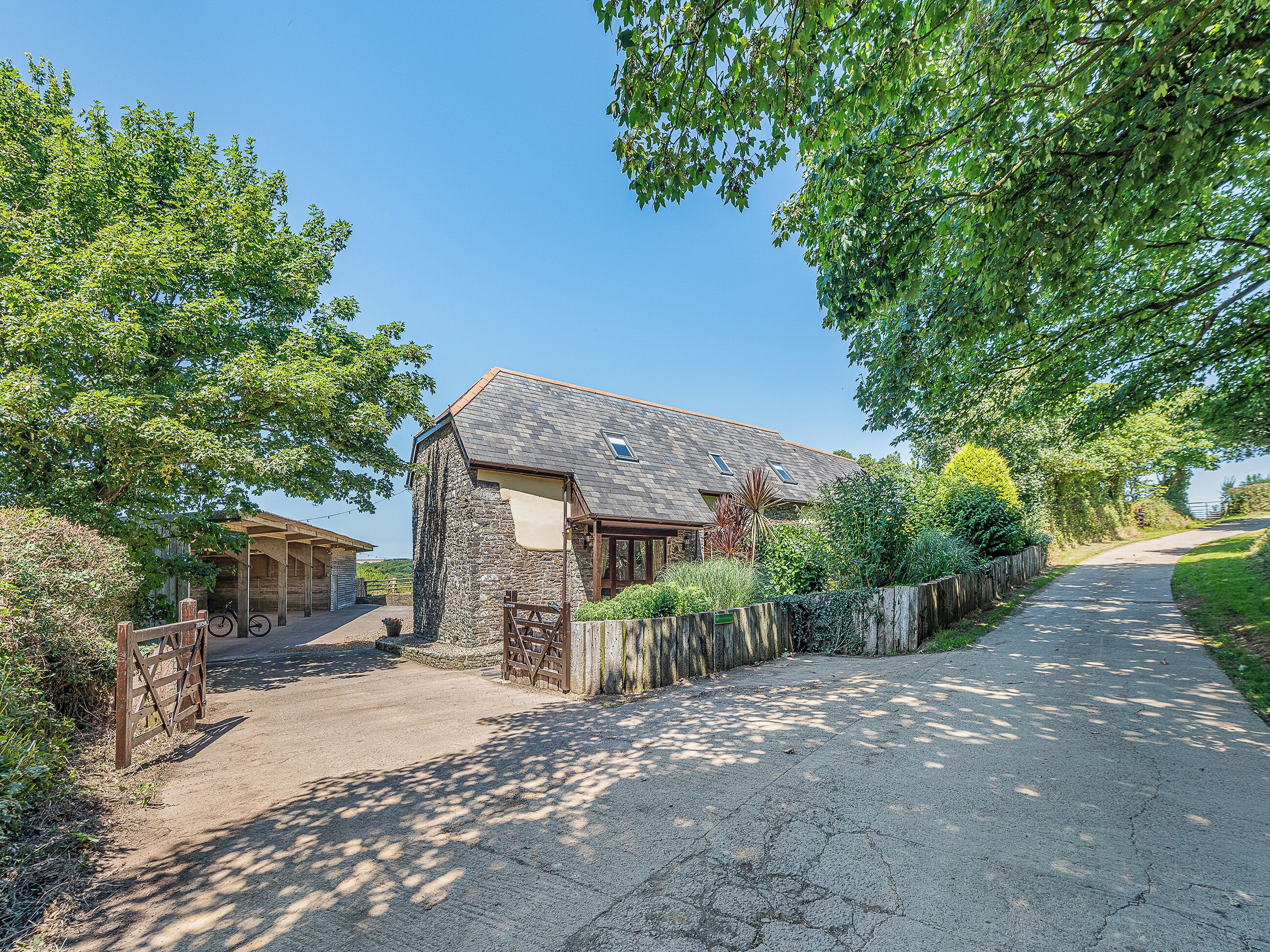 A stone house with a sloped roof, a covered porch, and a paved driveway.