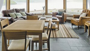 A spacious living area with a large window overlooking a body of water, a wooden dining table, and comfortable seating.